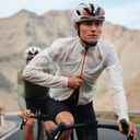 Ciclista con chaqueta cortavientos Velocio blanca, diseñada para ciclismo de ruta en carretera