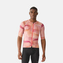 Ciclista con jersey Velocio ONE Artist GEO de tonos rosados y diseño geométrico, ajuste técnico y cremallera frontal.