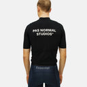 Vista trasera del jersey de ciclismo negro Pas Normal Studios Essential en un ciclista, mostrando logo y ajuste cómodo.
