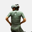 Ciclista con jersey verde oliva Pas Normal Studios Mechanism de Velo Store Mx, ajuste aerodinámico y bolsillos traseros
