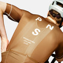 Ciclista con maillot marrón Pas Normal Studios Mechanism de corte aerodinámico y tejido técnico transpirable en Velo Store Mx