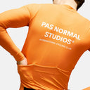 Ciclista con maillot de manga larga naranja Pas Normal Studios Mechanism, vista trasera con bolsillos reforzados.