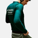Ciclista con maillot térmico verde de manga larga Pas Normal Studios Mechanism, ajuste aerodinámico y logo en espalda.