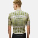 Ciclista de espaldas vistiendo el jersey Pas Normal Studios Essential en color Dot Bone con patrón de puntos verdes.